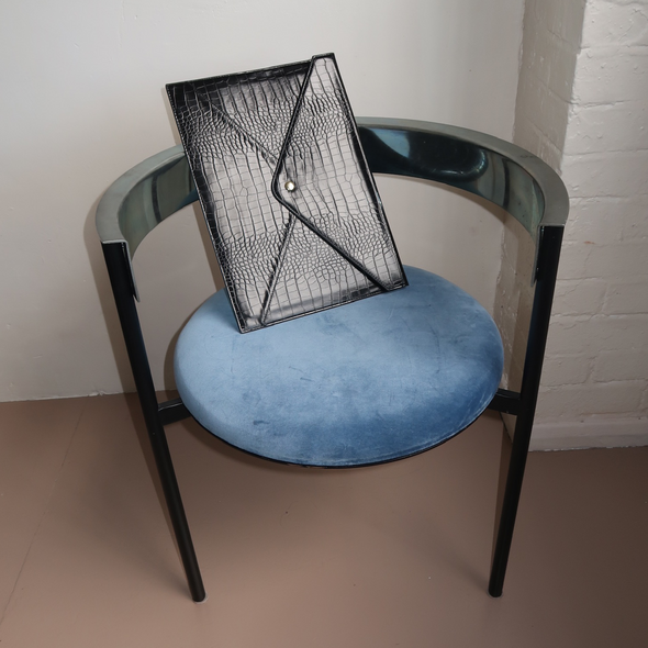 Blue chair with black leather laptop sleeve on it against a white brick wall.