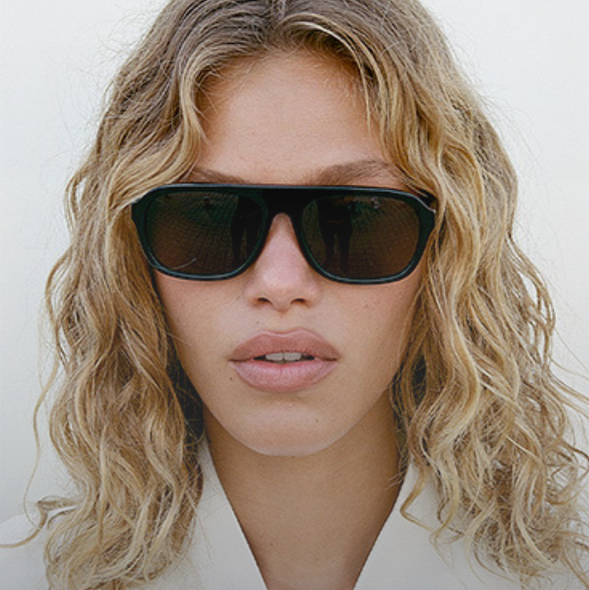 Woman wearing aviator style sunglasses with a neutral background